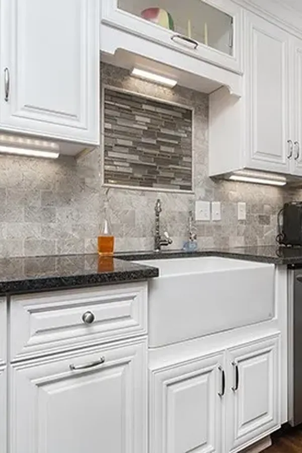 White raised panel cabinets with dark granite countertops and stacked stone backsplash