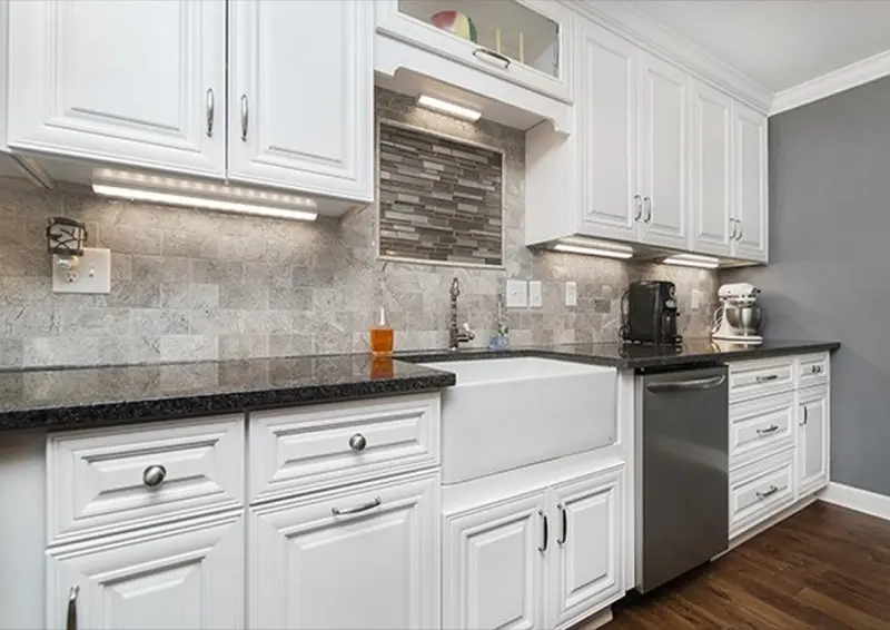 Close-up of a white shaker kitchen with granite countertop and glass tile backsplash