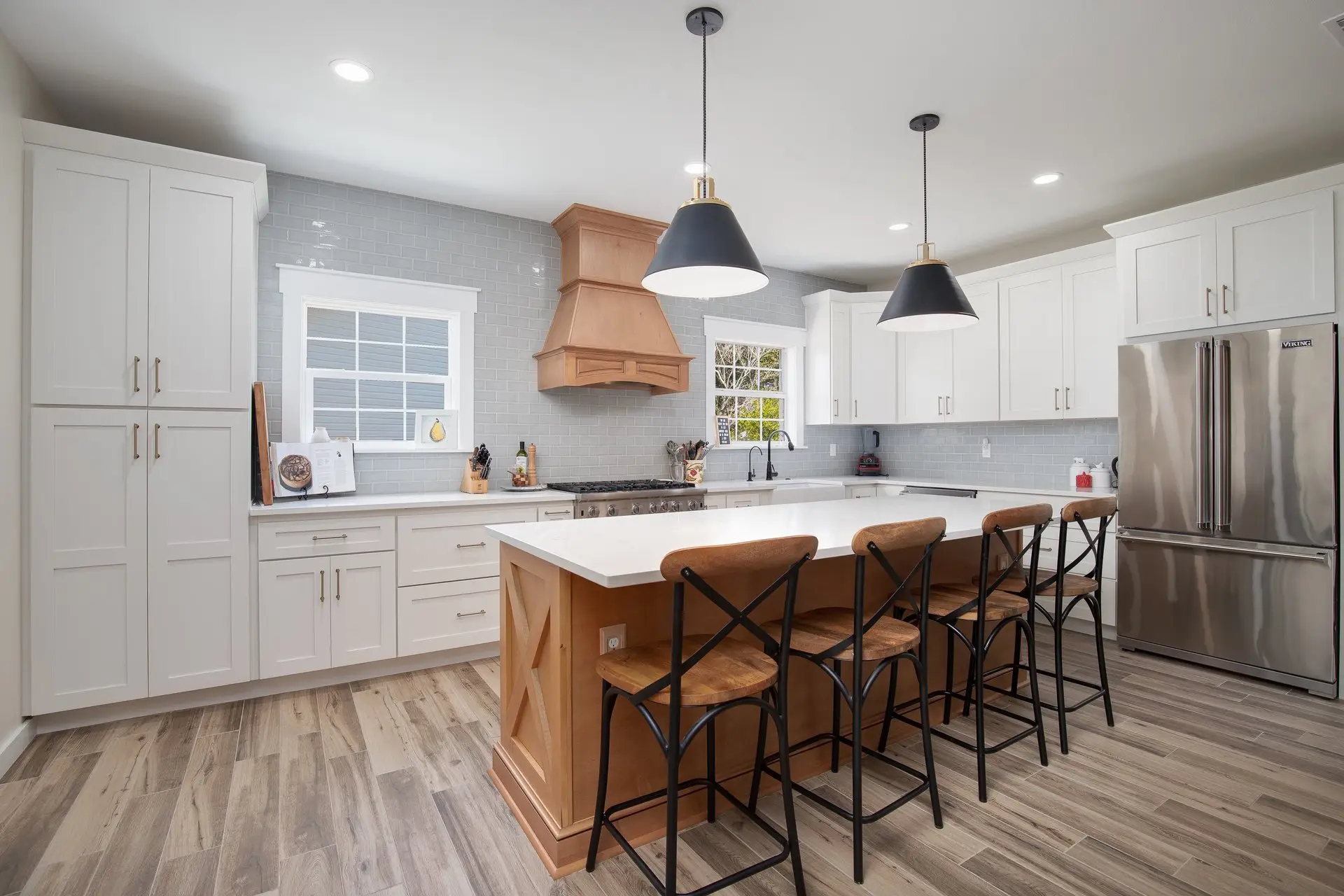 Bright white shaker kitchen renovation with wood range hood and island seating, built by Piloni Home Design