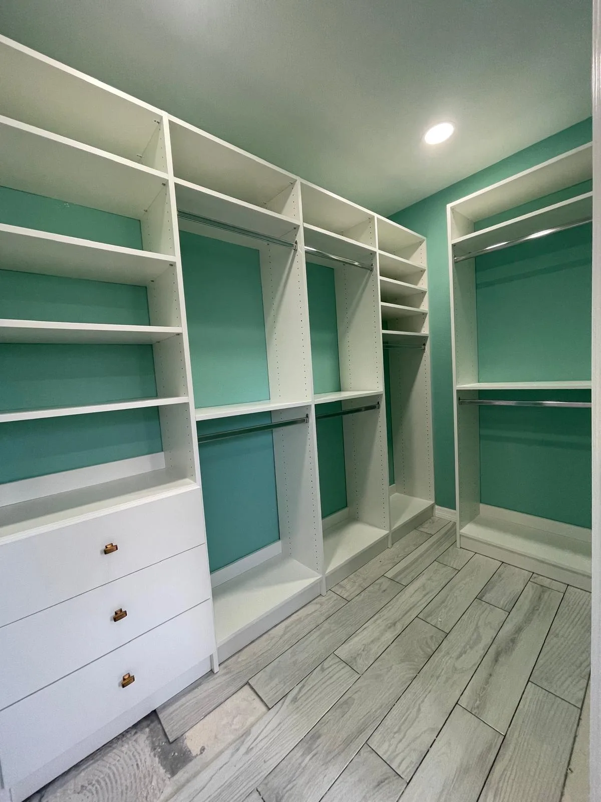Custom walk-in closet we built: white shelving and drawers against a mint green wall